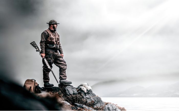Waterfowl hunter standing on a decoy-covered shoreline with shotgun in hand, representing Apex Ammunition’s dedication to precision and serious hunting.